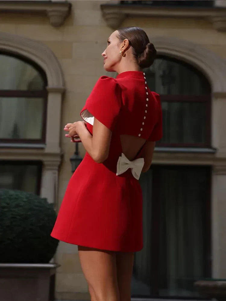  emale model showcasing a red mini dress with feminine bow detail on a plain background.ground.