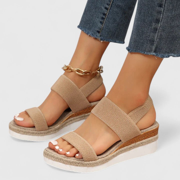  Woman wearing strappy wedge sandals with an elevated sole on a plain background.