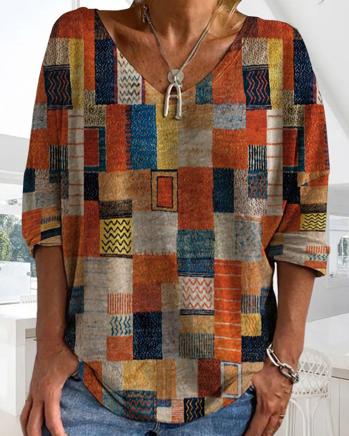  Female showcasing a colorful patchwork top with a flattering V-neck design on a plain background.