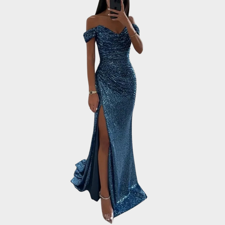Female model wearing an elegant open shoulder evening dress with front slit on a plain background.