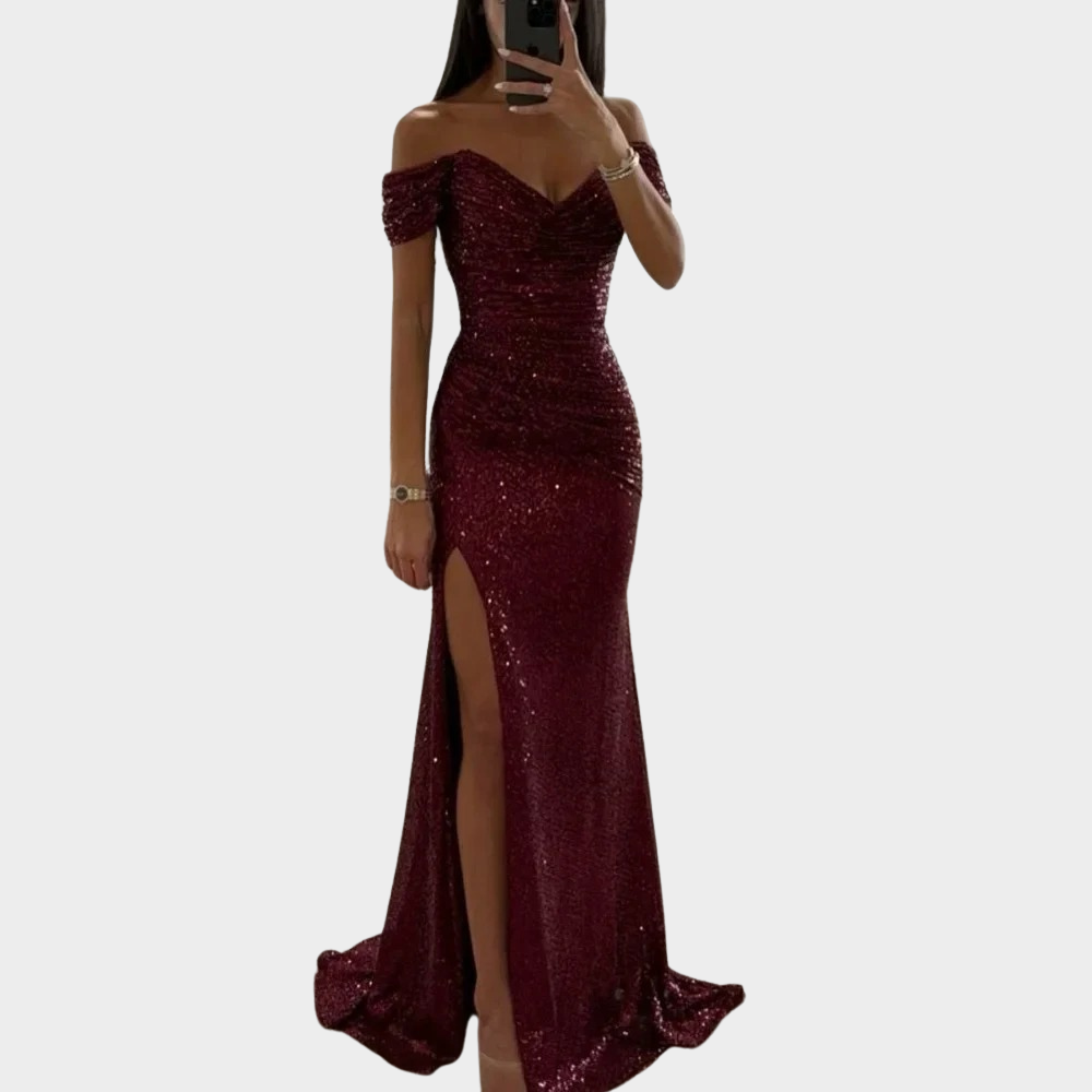 Model wearing a graceful long evening dress with subtle shine and front slit on a plain background.