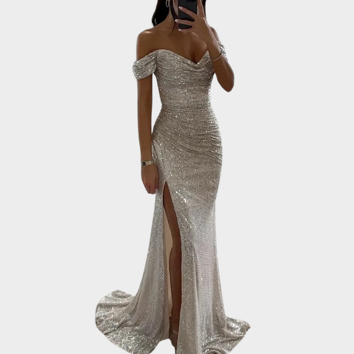 Female model in an open shoulder formal dress with fitted shape on a plain background.