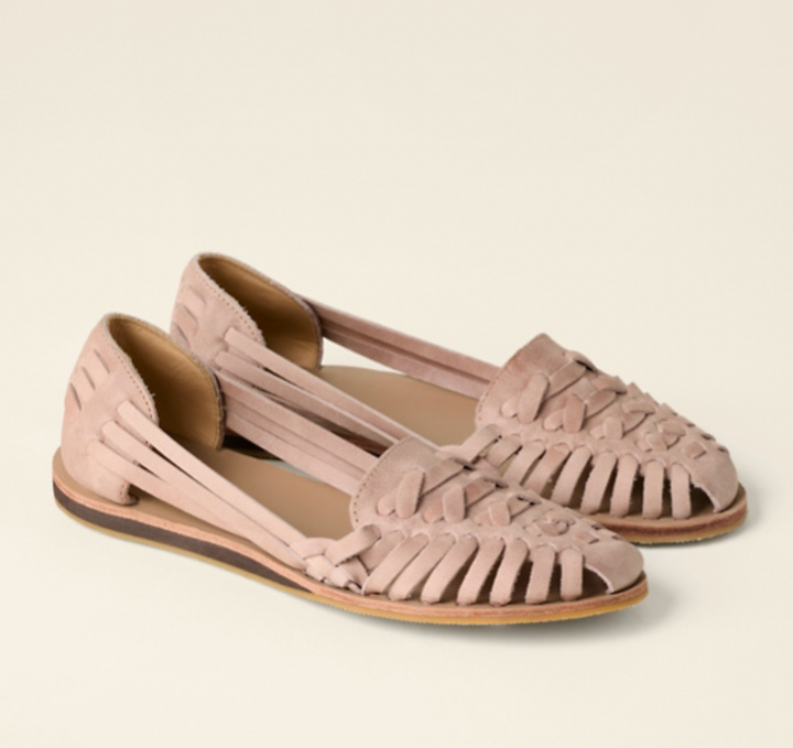  Female model standing in flat woven shoes on a plain background.