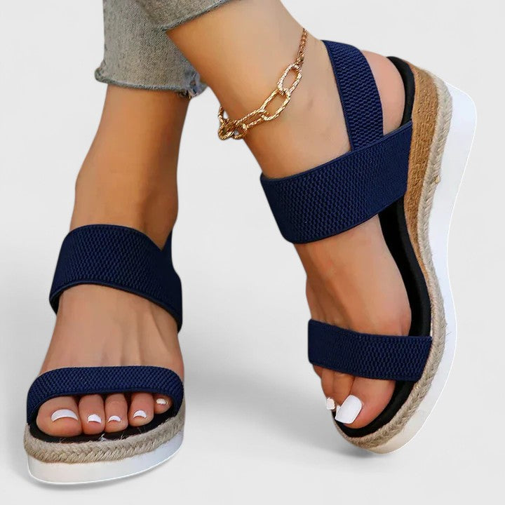  Woman displaying fashionable wedge sandals with a secure ankle strap on a plain background.