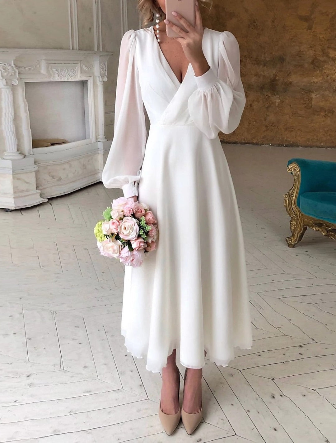 Woman wearing flowing long sleeve formal dress on plain gray background.