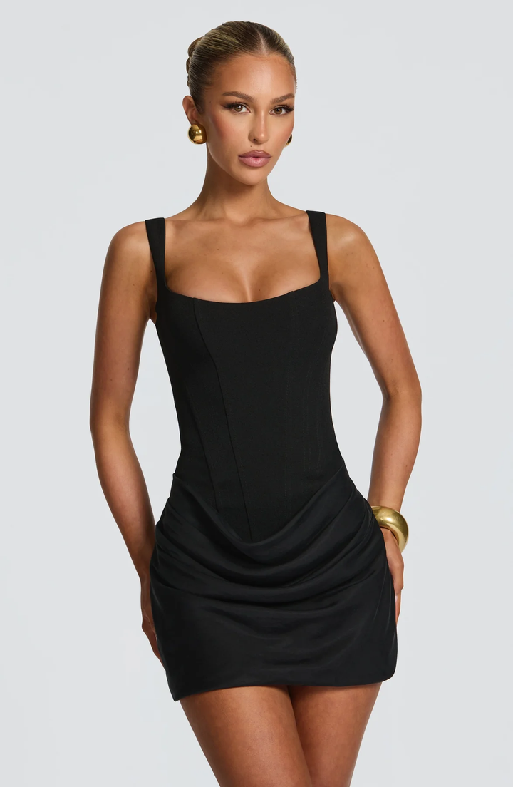  Woman wearing a fitted mini dress featuring a clean neckline and elegant drape on a plain background.