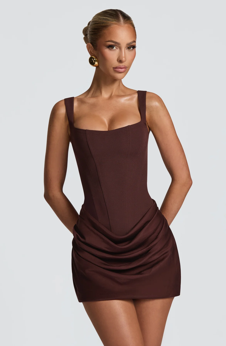 Woman showcasing a modern mini dress with a square neckline and soft skirt movement on a plain background.