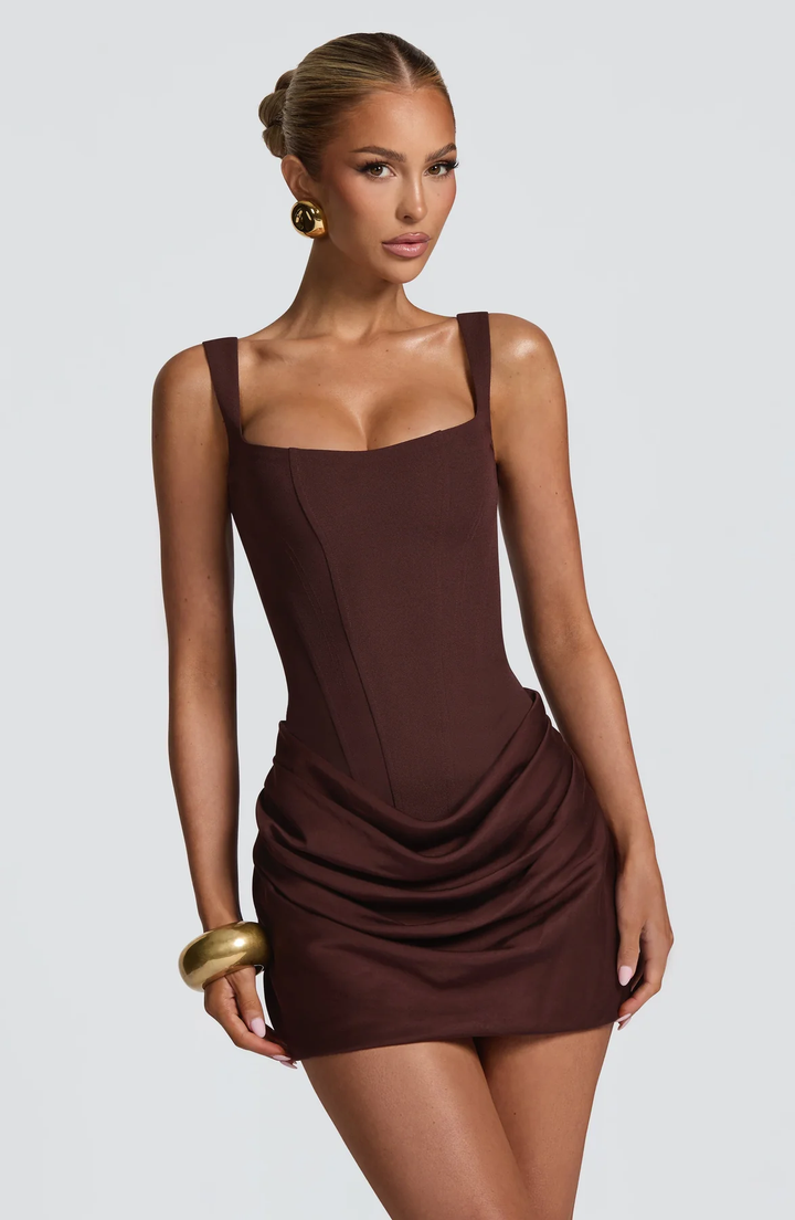  Woman wearing a contemporary mini dress with elegant draped detailing on a plain background.