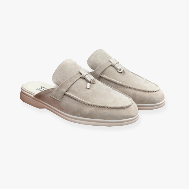 Woman styling backless mule shoes on a plain background with relaxed outfit appeal.