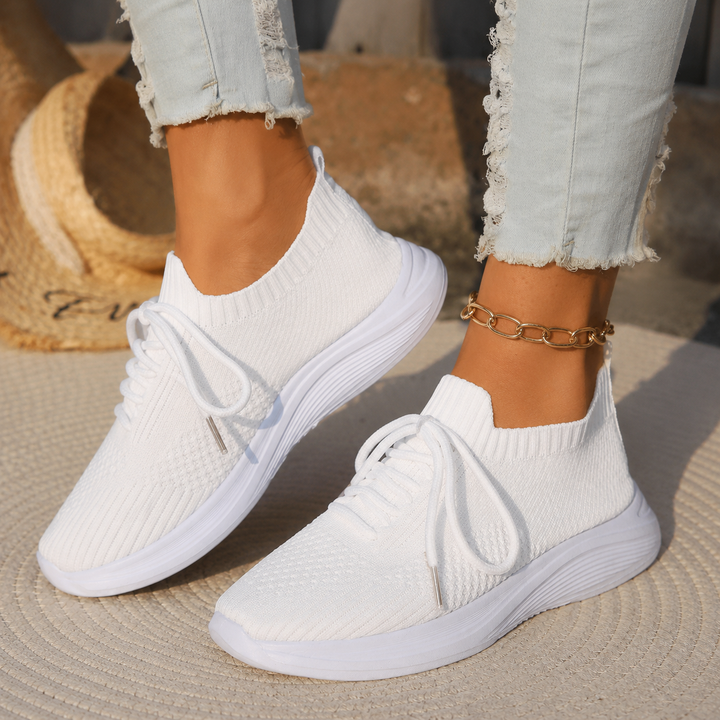 Woman showcasing flexible casual sneakers with a clean plain backdrop.