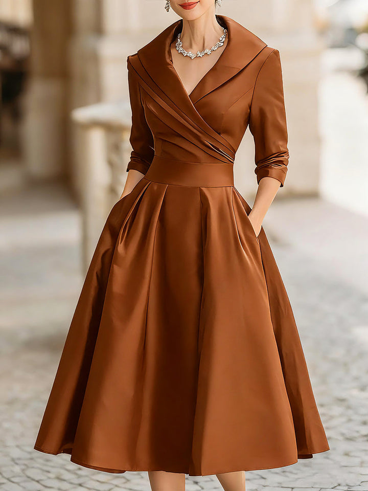 Female model in a flowing A line midi dress with a defined waist on a plain background.