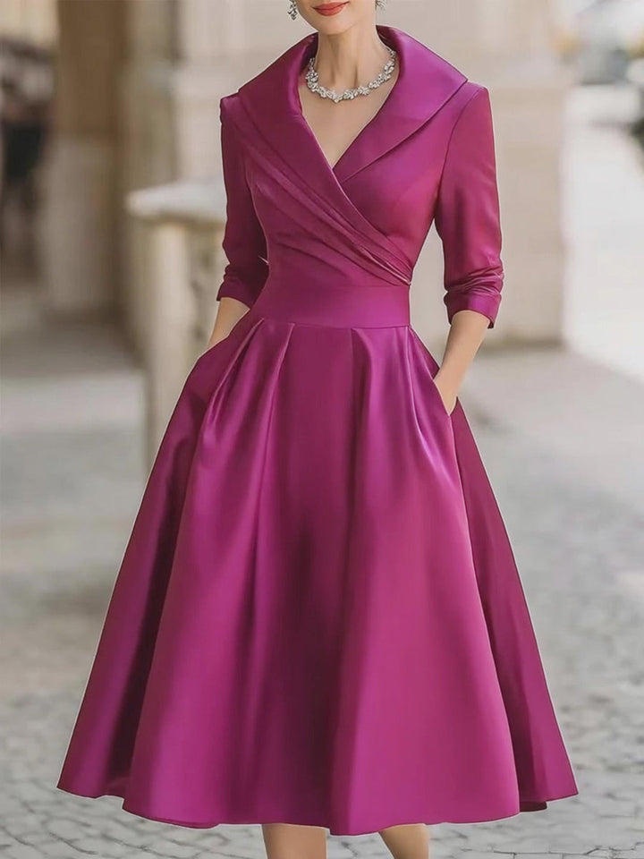Model in an elegant midi dress with a defined waist and soft drape against a plain background.