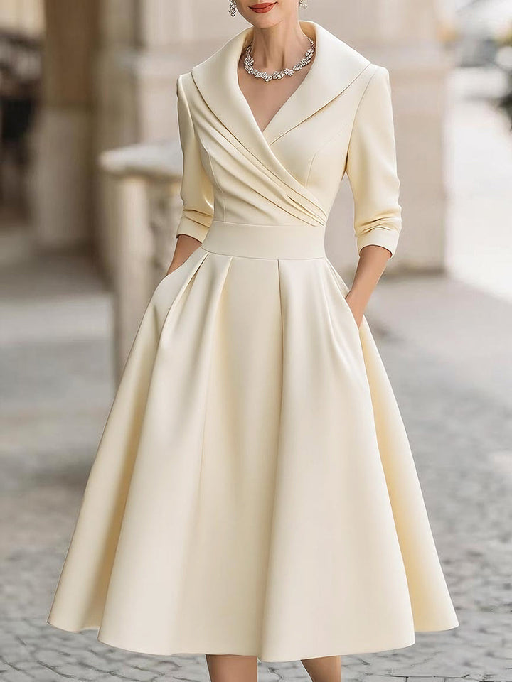 Woman in a vintage style midi dress with a shawl collar and polished silhouette on a plain background.