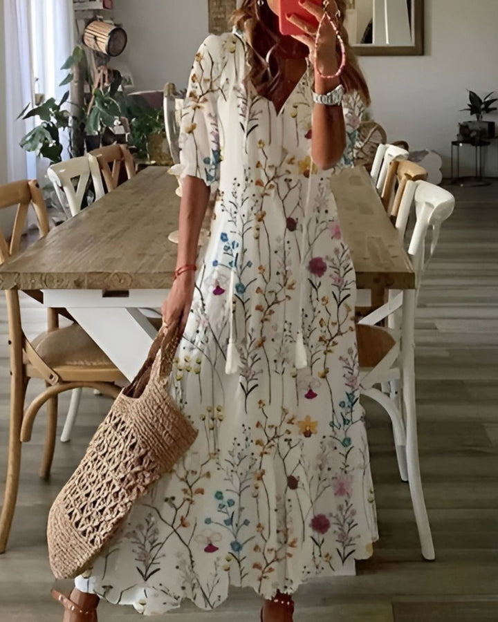 Female wearing a flowy printed dress with tassel accents on a plain background.