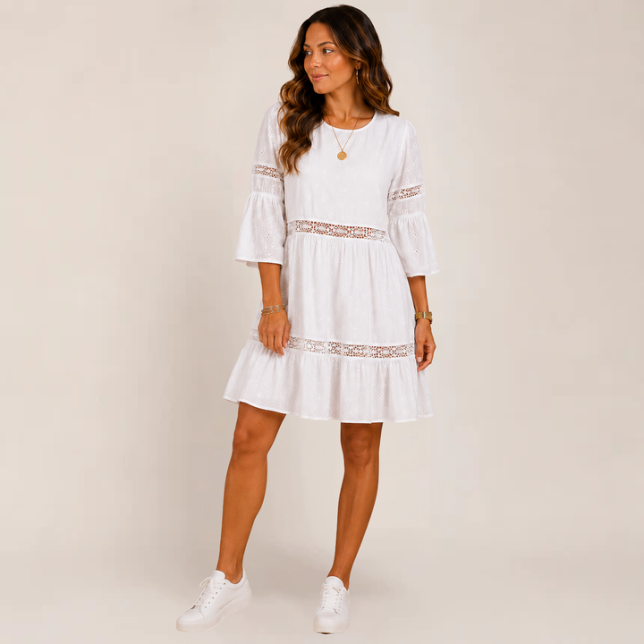 Female model wearing a feminine summer sundress with a flowing skirt on a plain background.