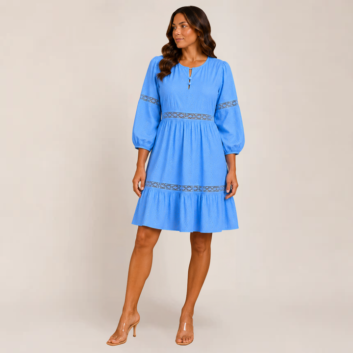 Woman in a relaxed tiered sundress with soft movement and 3/4 sleeves on a plain background.