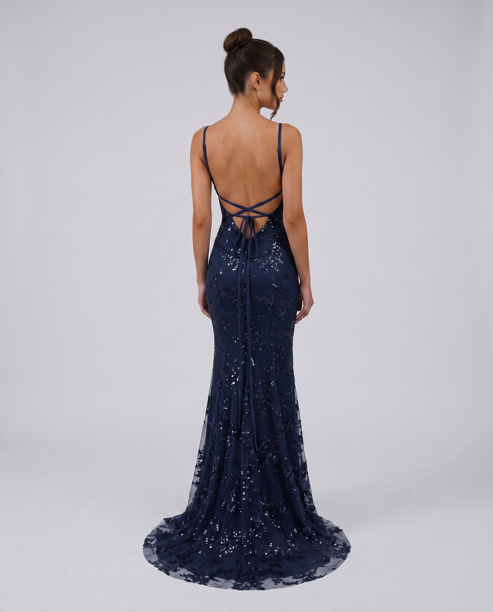 Woman wearing a navy embellished maxi gown with slim straps on a plain background.