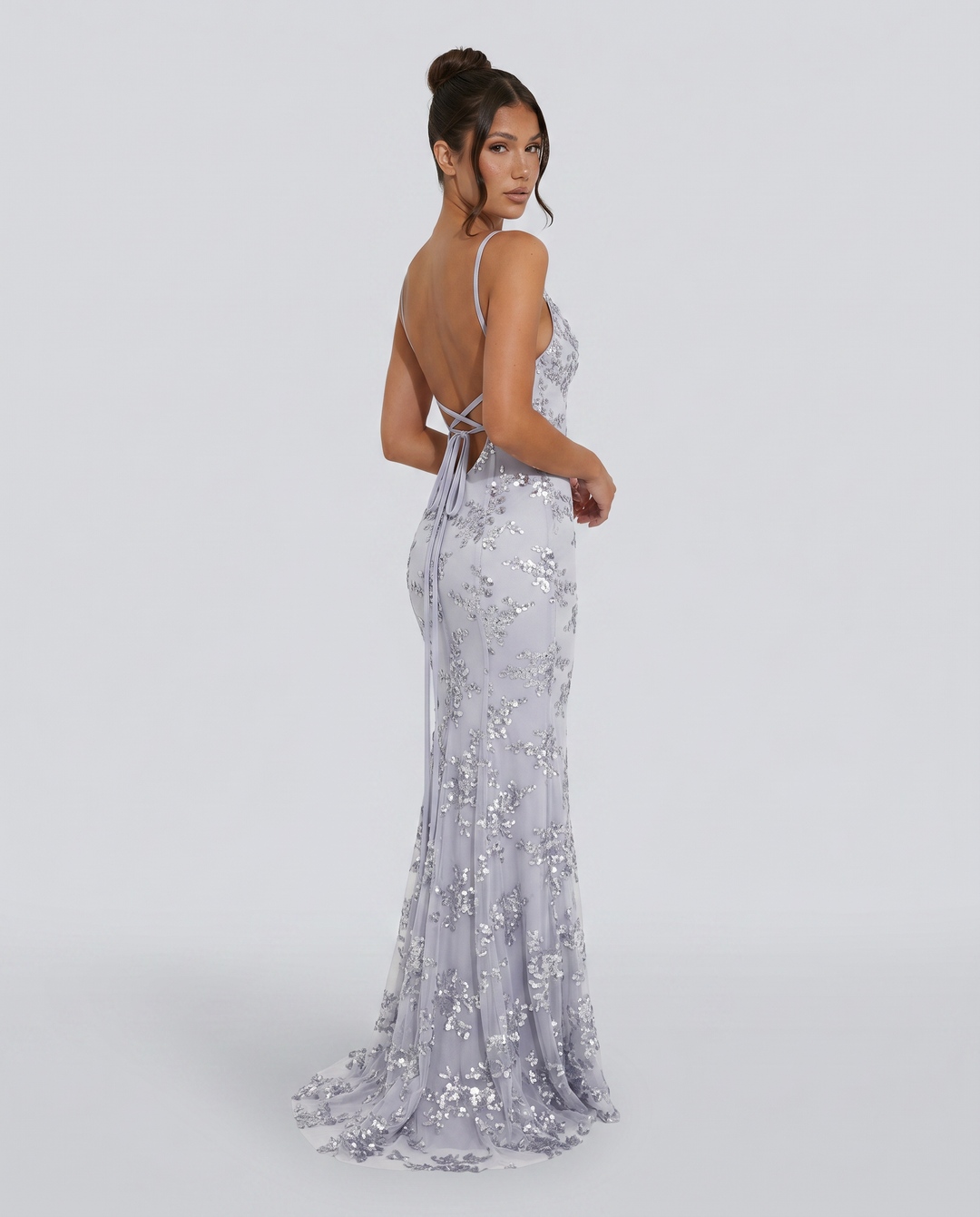 Woman wearing a fitted embellished gown with low back and flared hem on a plain background.