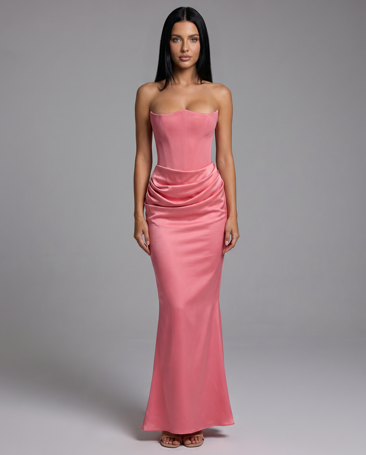 Woman wearing a fitted strapless dress with a flowing maxi skirt on a plain background.