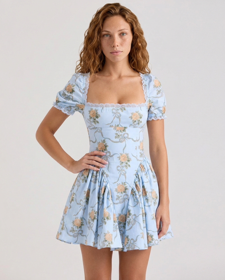 Woman standing in a floral mini dress with a fitted waist and flared skirt on a plain background.