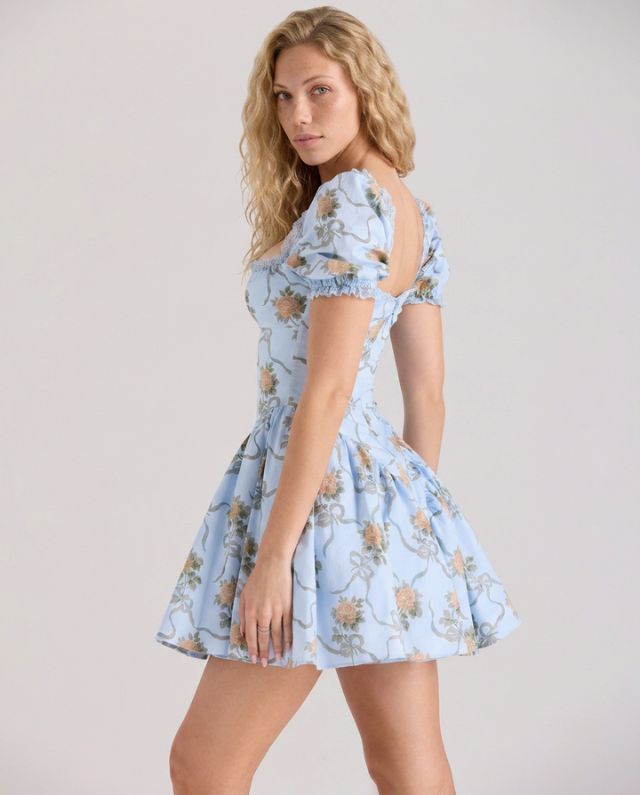 Female model in a yellow floral mini dress with a square neckline on a plain background.