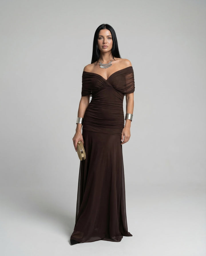 Woman presenting an evening dress with a gathered waist on a plain background.
