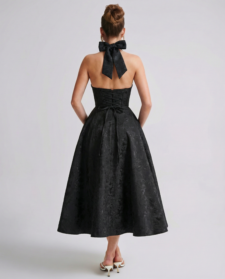 Woman in a halter neck midi dress with an open back against a plain backdrop