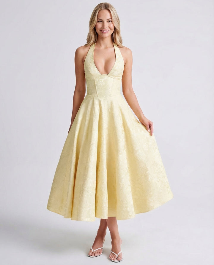Female wearing a sleeveless halter midi dress with a flared skirt against a plain background.