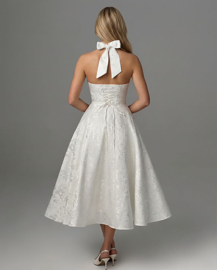 Woman posing in a sleeveless occasion dress with a halter neckline and midi length.