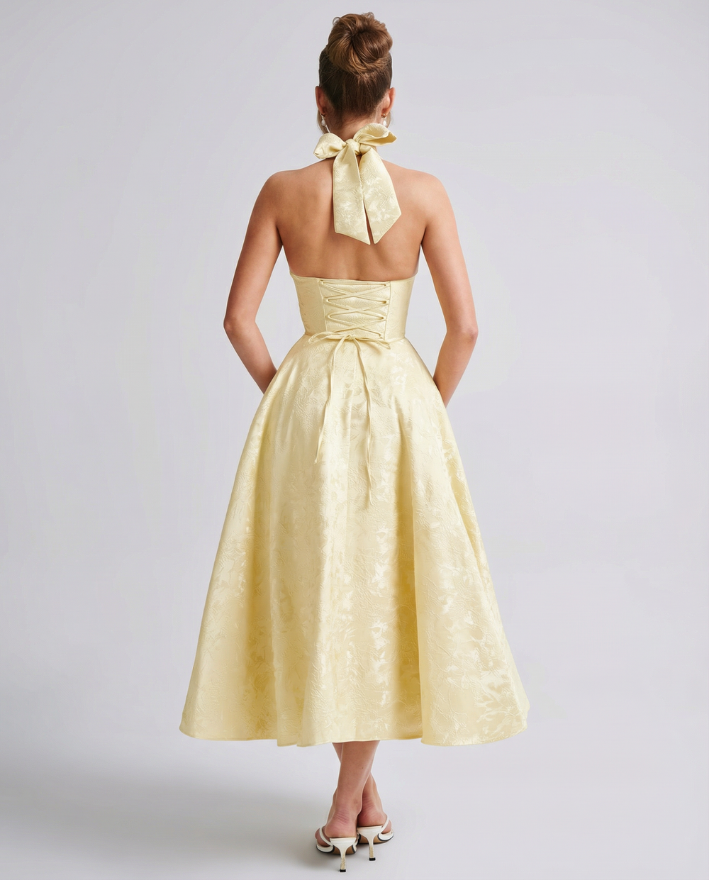 Woman in a textured midi dress with an open back and lace-up detail on a plain background.