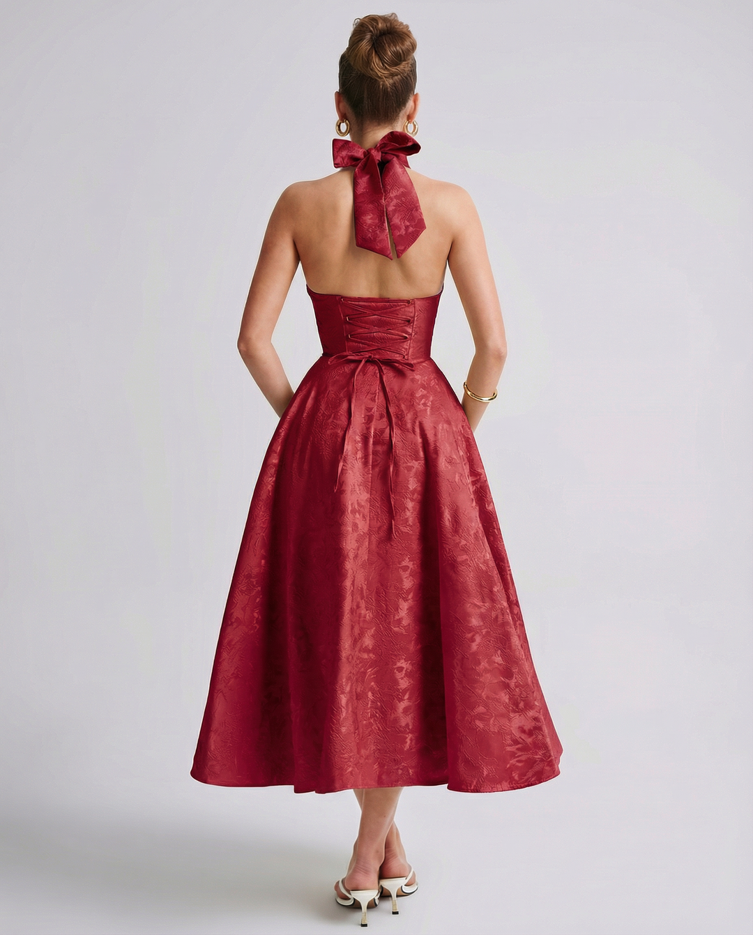 Woman wearing a structured midi dress with lace-up back detailing on a plain background.