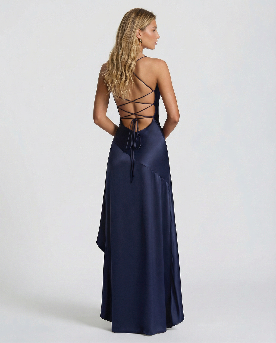 Woman showcasing a sleeveless maxi dress with asymmetrical overlay on a plain background.