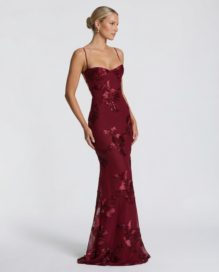 Woman styled in a fitted sleeveless gown with floral appliqué detailing and lace-up back.