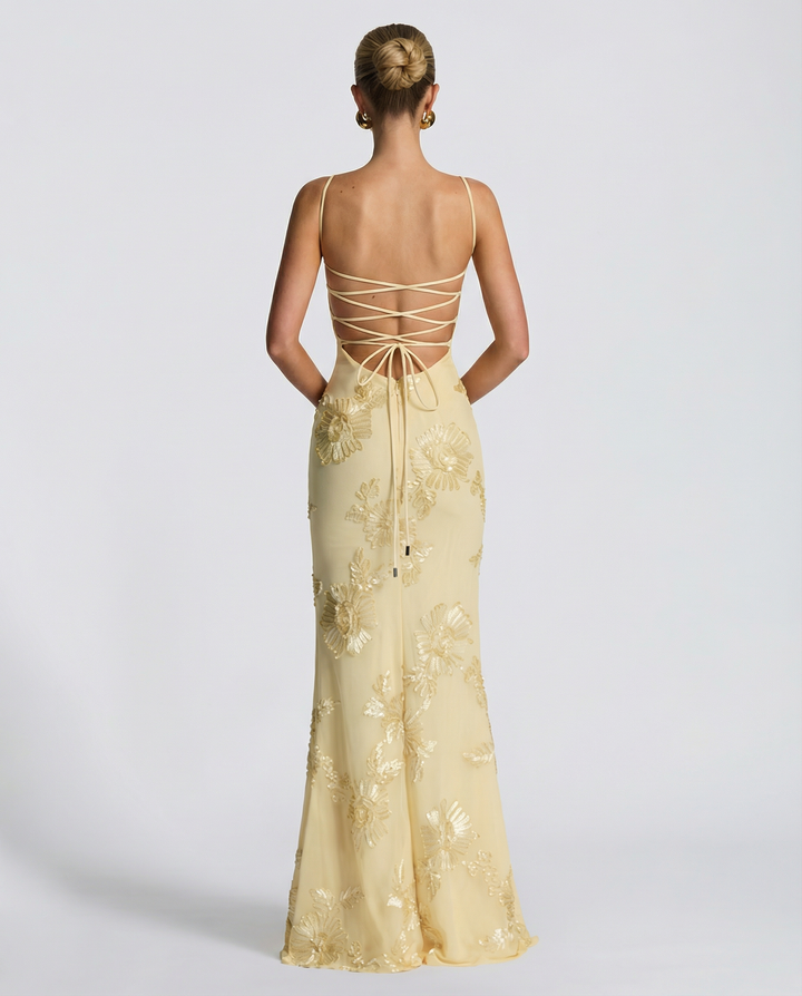 Model posing in a full-length fitted dress with floral detailing and slim straps.
