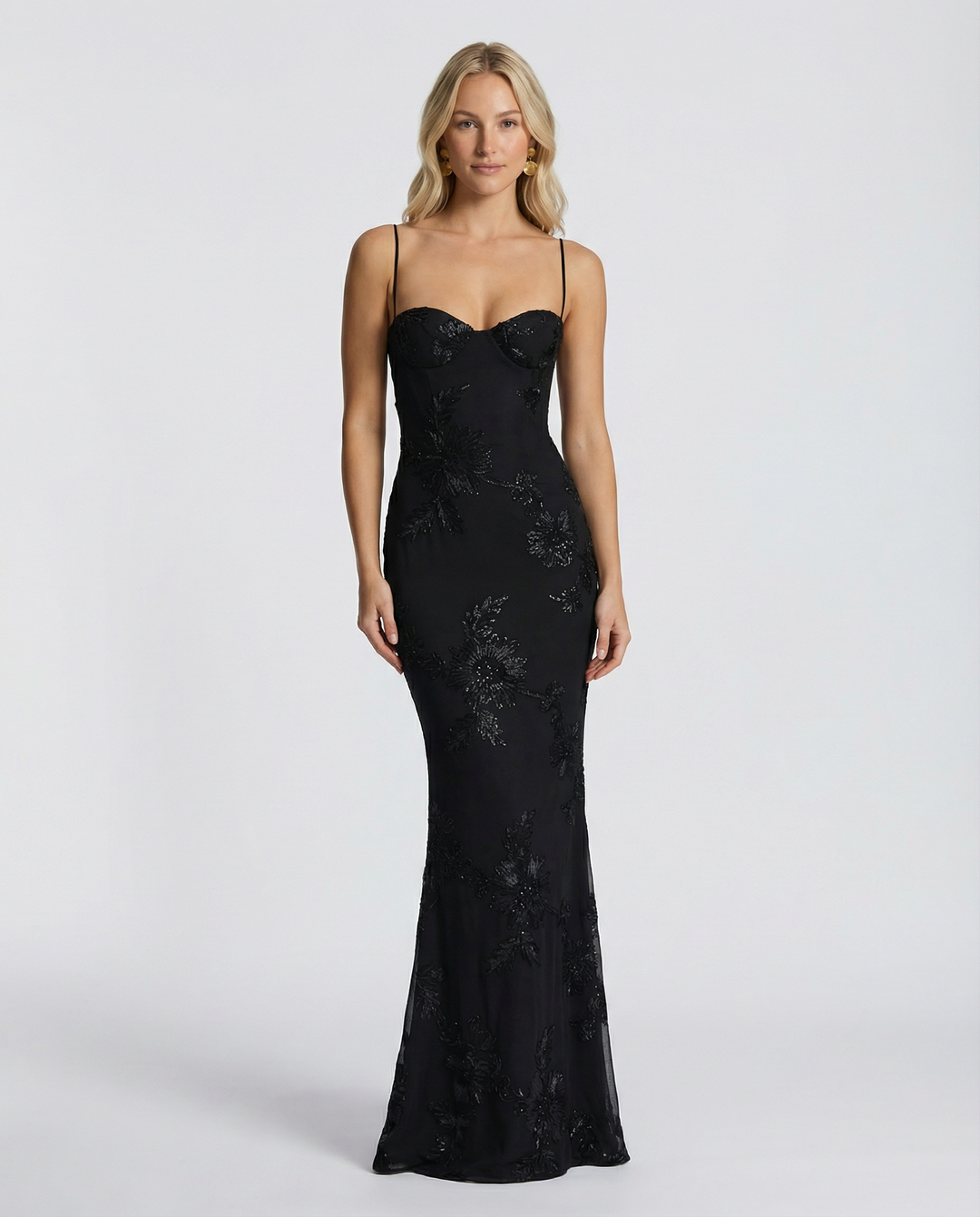 Model wearing a fitted formal maxi dress with floral appliqué and slim shoulder straps.