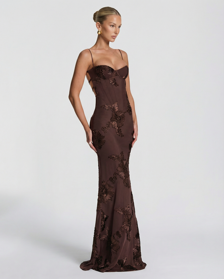 Woman posing in a sleek floral appliqué maxi dress against a clean plain background.