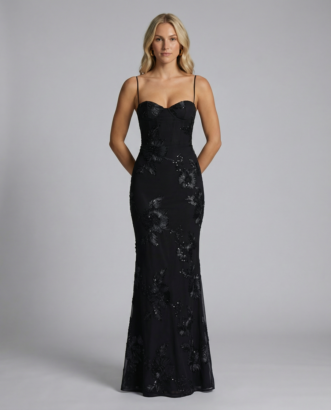Female wearing a long floral appliqué dress with sweetheart neckline and fitted shape.