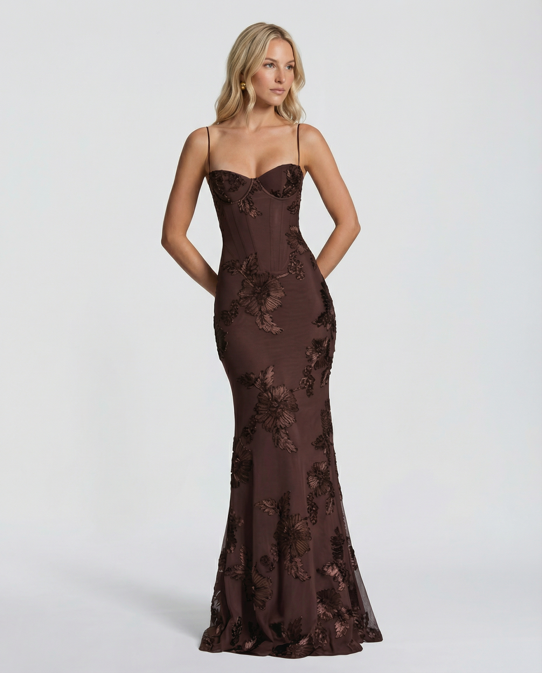 Female model wearing a full-length occasion dress with fitted bodice and floral accents.
