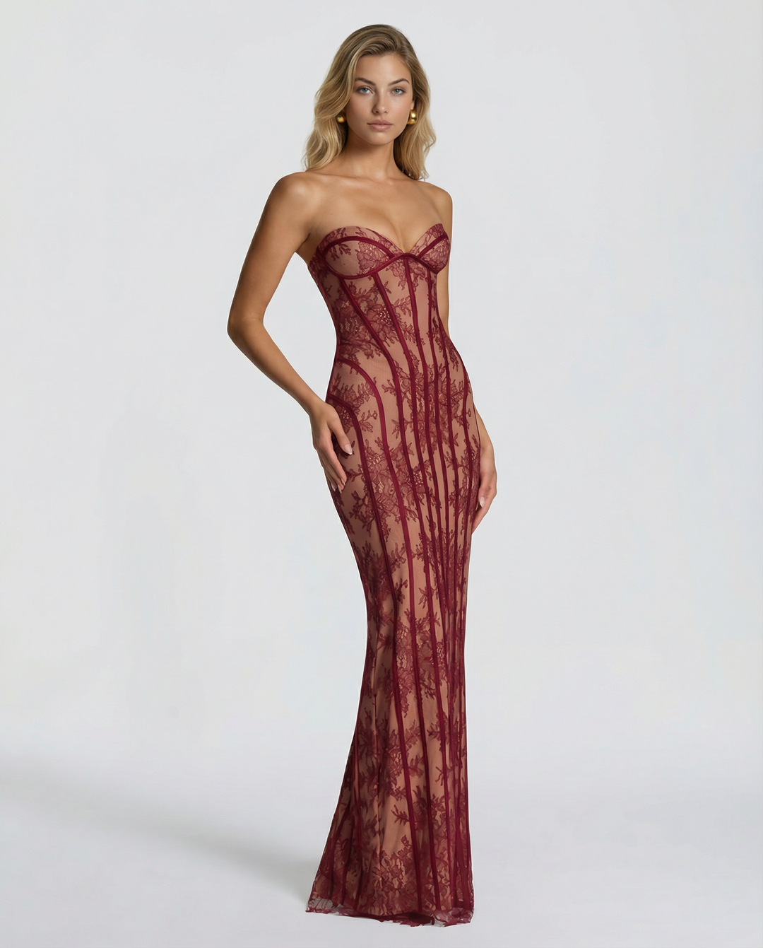 Woman wearing a strapless sheer lace corset maxi dress on a plain background.