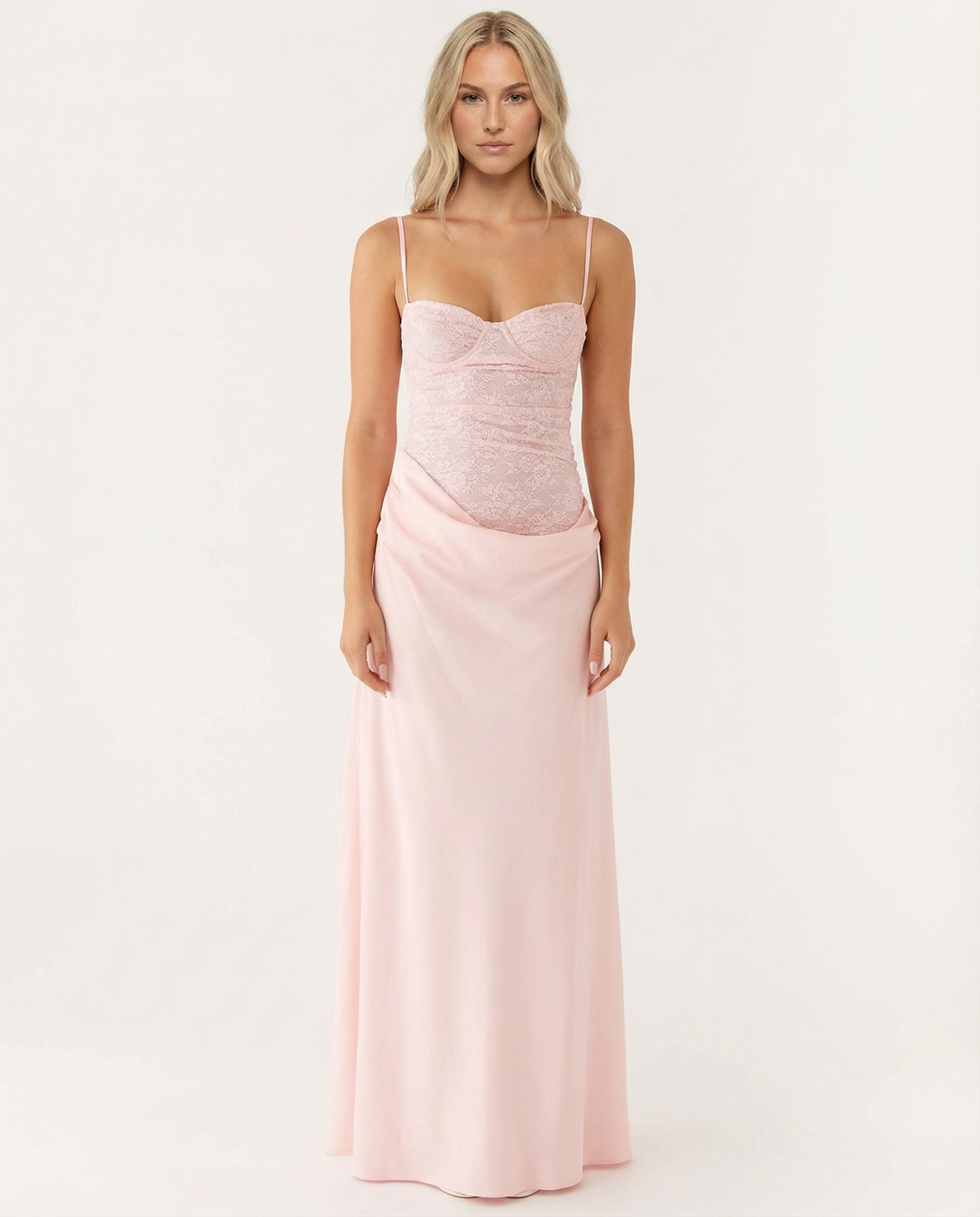 Woman wearing a pink maxi dress with a sweetheart neckline and draped hip detail on a plain background.