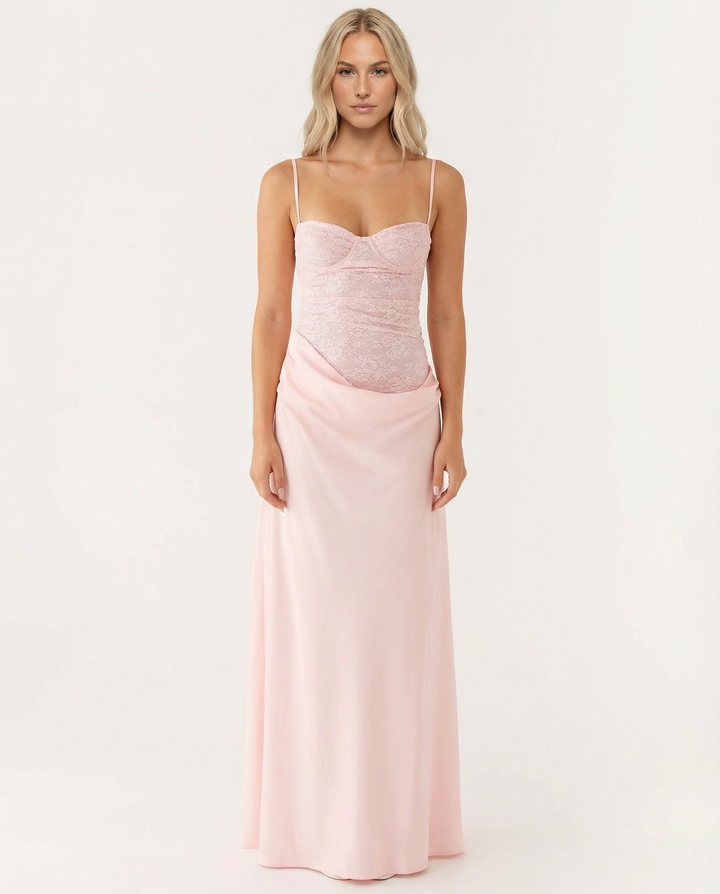 Woman wearing a pink maxi dress with a sweetheart neckline and draped hip detail on a plain background.