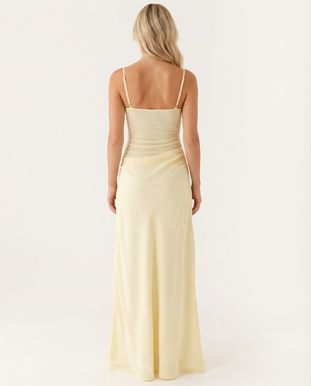 Woman wearing a yellow evening maxi dress with cowl hip draping on a plain background.