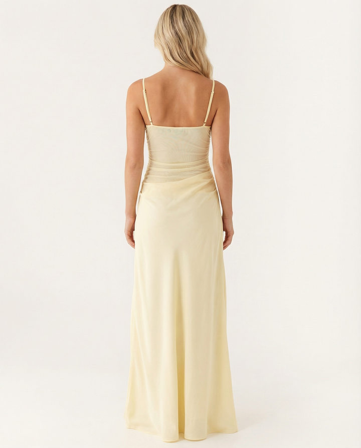 Woman wearing a yellow evening maxi dress with cowl hip draping on a plain background.
