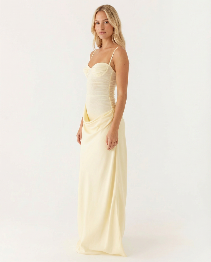 Model in a sleeveless pink maxi dress with structured bust and flowing skirt on a plain background.