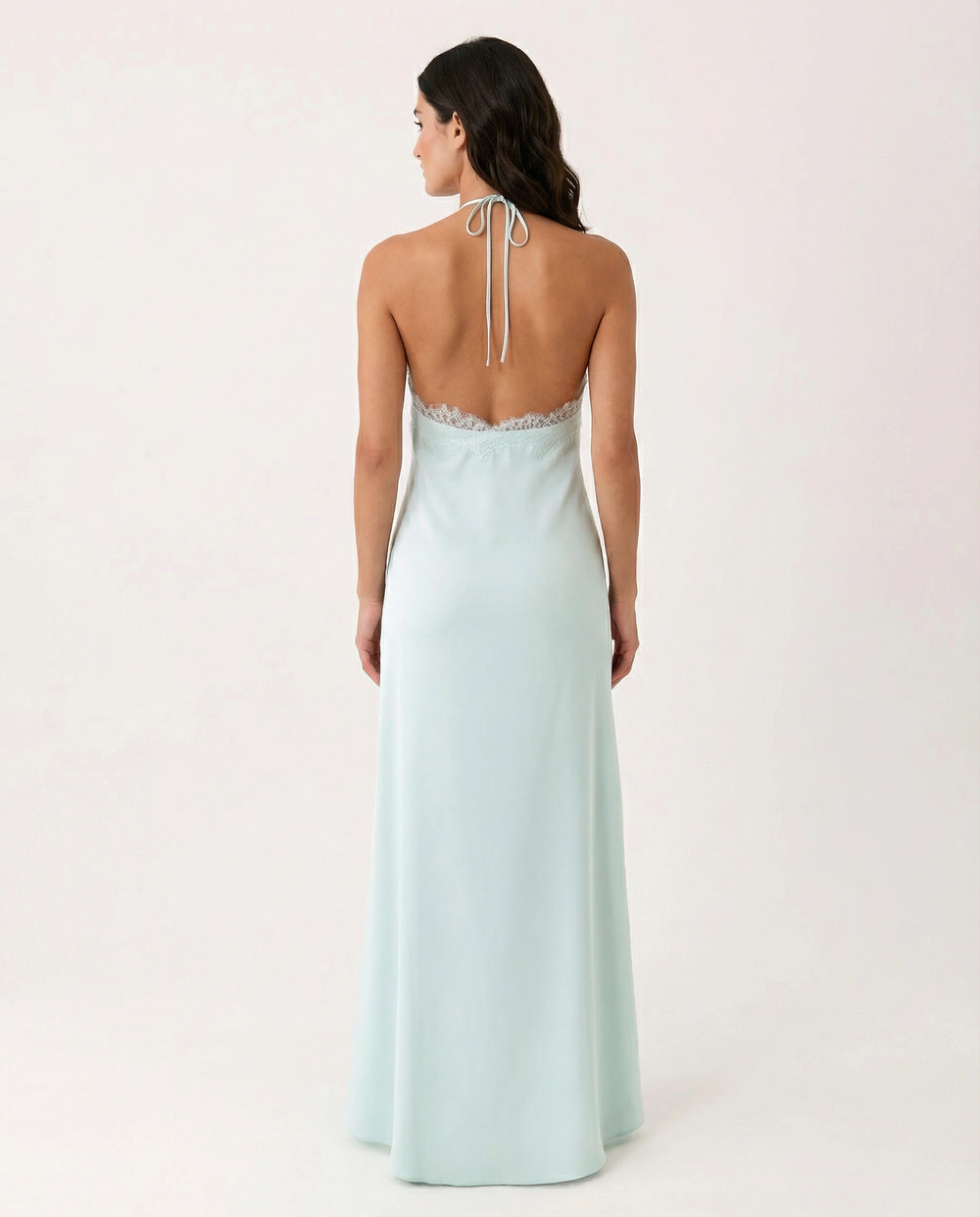Woman in a flowing blue sleeveless maxi dress with halter neckline on a plain background.