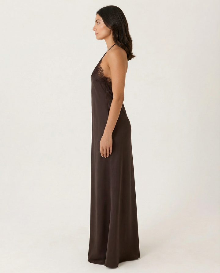 Woman in a open back maxi dress styled with minimal accessories on a plain background.