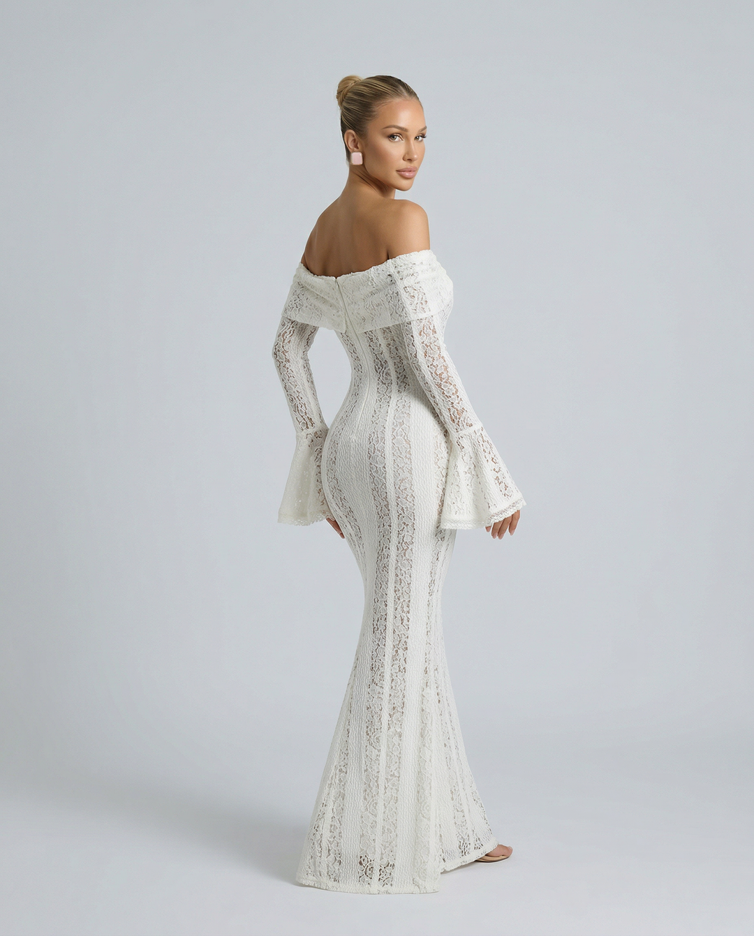 Female model in a white off shoulder evening dress with flared hem on a plain background.