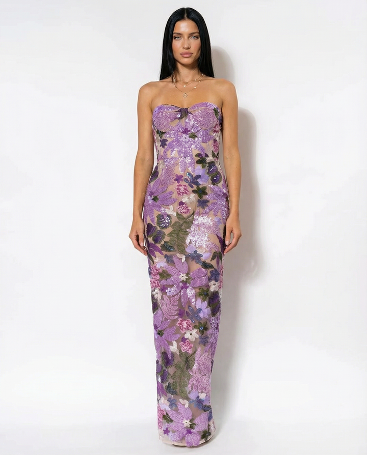 Woman posing in a purple strapless floral sequin dress with fitted waist on a plain background.