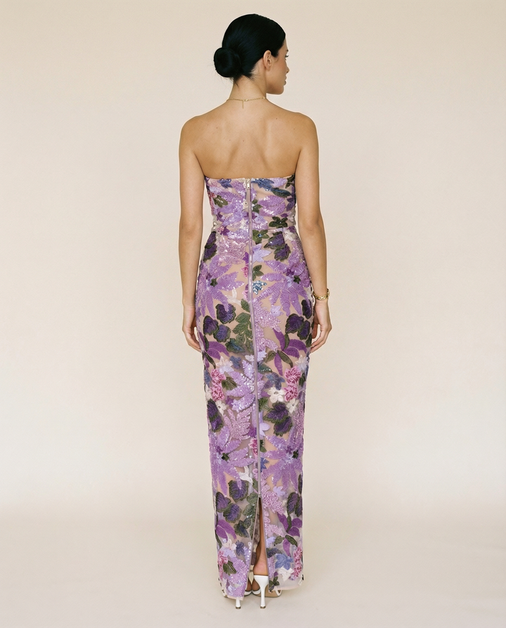 Woman wearing a purple strapless maxi dress with floral sequin embroidery on a plain background.