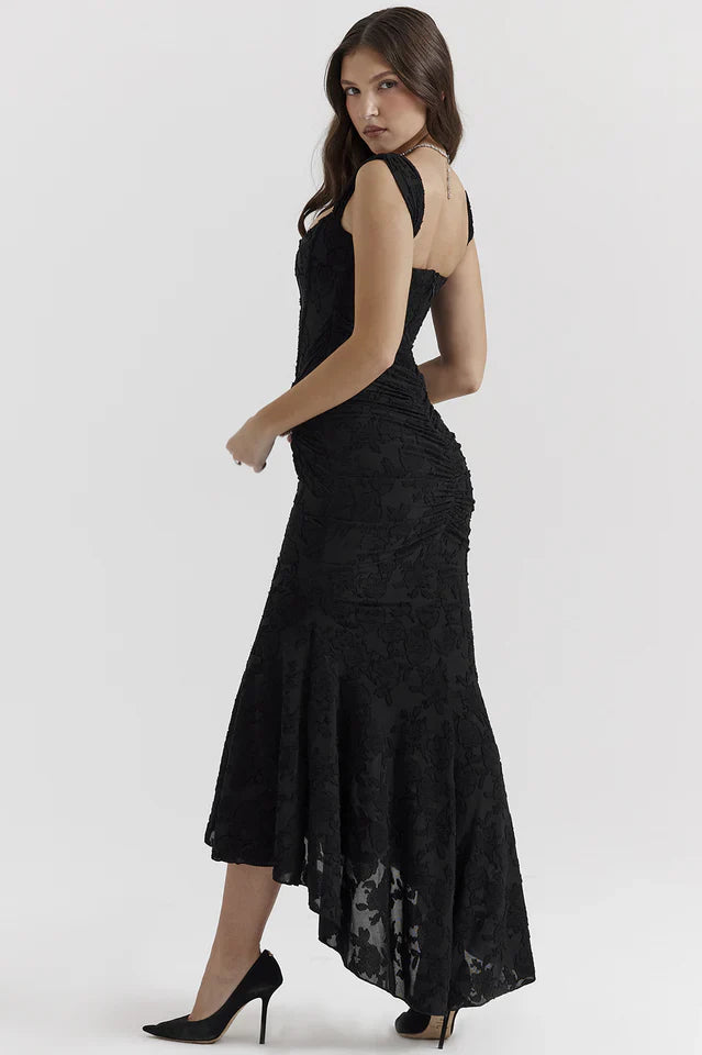 Female model in a fitted black evening dress with flared hem against a plain background.